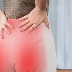 Kobieta trzymająca się za bolące biodro, z zaznaczonym na czerwono obszarem bólu.