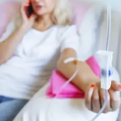 Kobieta z kroplówką w ręku rozmawia przez telefon.