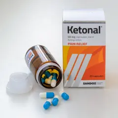 Pudełko i butelka leku Ketonal z kapsułkami na białym tle.