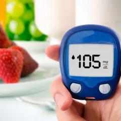 Dłoń trzyma glukometr pokazujący 105 mg/dL, w tle truskawki i napoje.