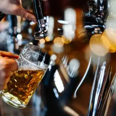 Ręka nalewa piwo do kufla z kranu barmańskiego.