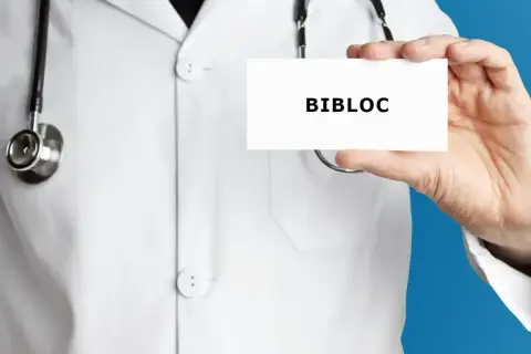 Lekarz w białym kitlu trzyma kartkę z napisem "BIBLOC". To nazwa handlowa leku bisoprolol, stosowanego w leczeniu chorób serca.