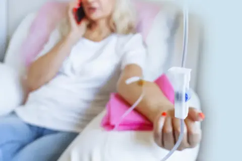 Kobieta z kroplówką w ręku rozmawia przez telefon.