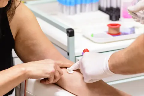 Pobieranie krwi do badań. Ręka pacjentki z wacikiem, ręka pielęgniarki w rękawiczce z igłą i probówką MPV.