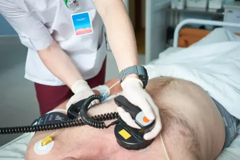 Ratownik medyczny wykonuje kardiowersję pacjentowi w szpitalu, używając defibrylatora.