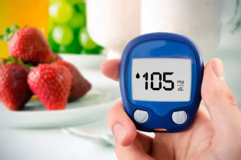Dłoń trzyma glukometr pokazujący 105 mg/dL, w tle truskawki i napoje.