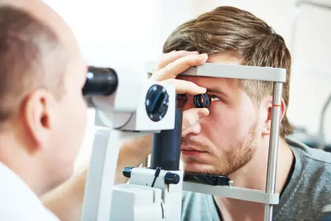Lekarz wykonuje badanie dna oka młodego mężczyzny za pomocą specjalistycznego sprzętu.
