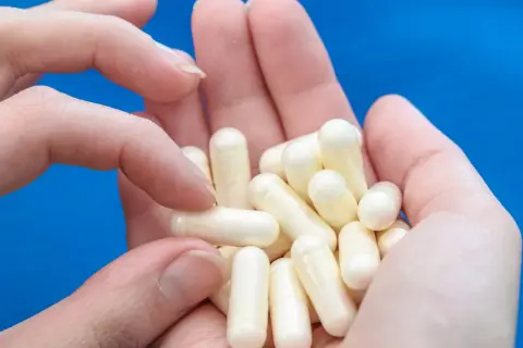 Dłonie trzymają garść białych kapsułek. To biotyna tabletki, które pomagają zadbać o włosy i paznokcie.