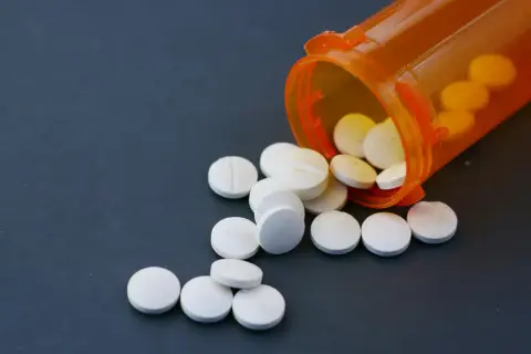 Białe tabletki rozsypane z pomarańczowego pojemnika. Niektóre z nich mogą zawierać fentanyl, substancję o silnym działaniu.