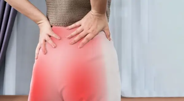 Kobieta trzymająca się za bolące biodro, z zaznaczonym na czerwono obszarem bólu.