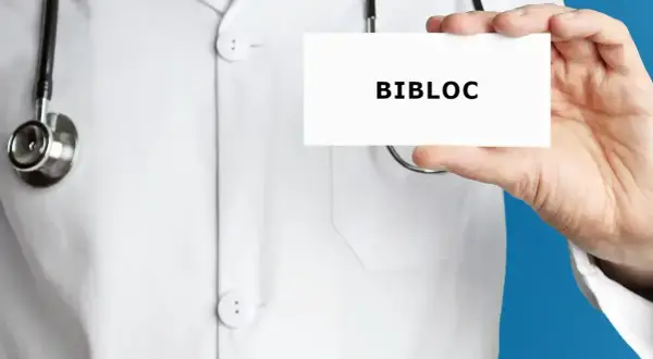 Lekarz w białym kitlu trzyma kartkę z napisem "BIBLOC". To nazwa handlowa leku bisoprolol, stosowanego w leczeniu chorób serca.