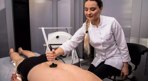 Fizjoterapeutka wykonuje kriolezję stawu biodrowego u pacjenta leżącego na kozetce.