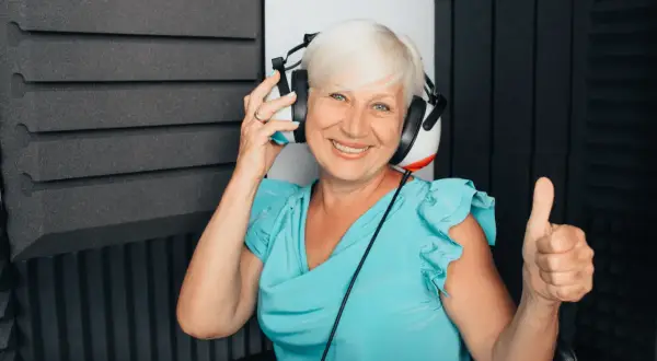 Uśmiechnięta kobieta w słuchawkach podczas badania audiometrii tonalnej. Pokazuje kciuk w górę, co oznacza pozytywny wynik.