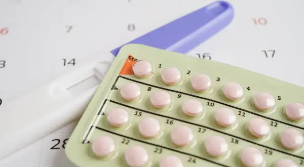 Test ciążowy i blister tabletek antykoncepcyjnych na tle kalendarza. Decyzje o płodności, planowanie rodziny, vixpo.
