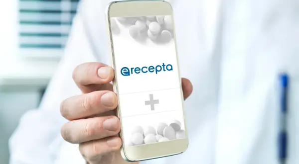 Dłoń trzyma smartfon z logo e-recepty i pigułkami.
