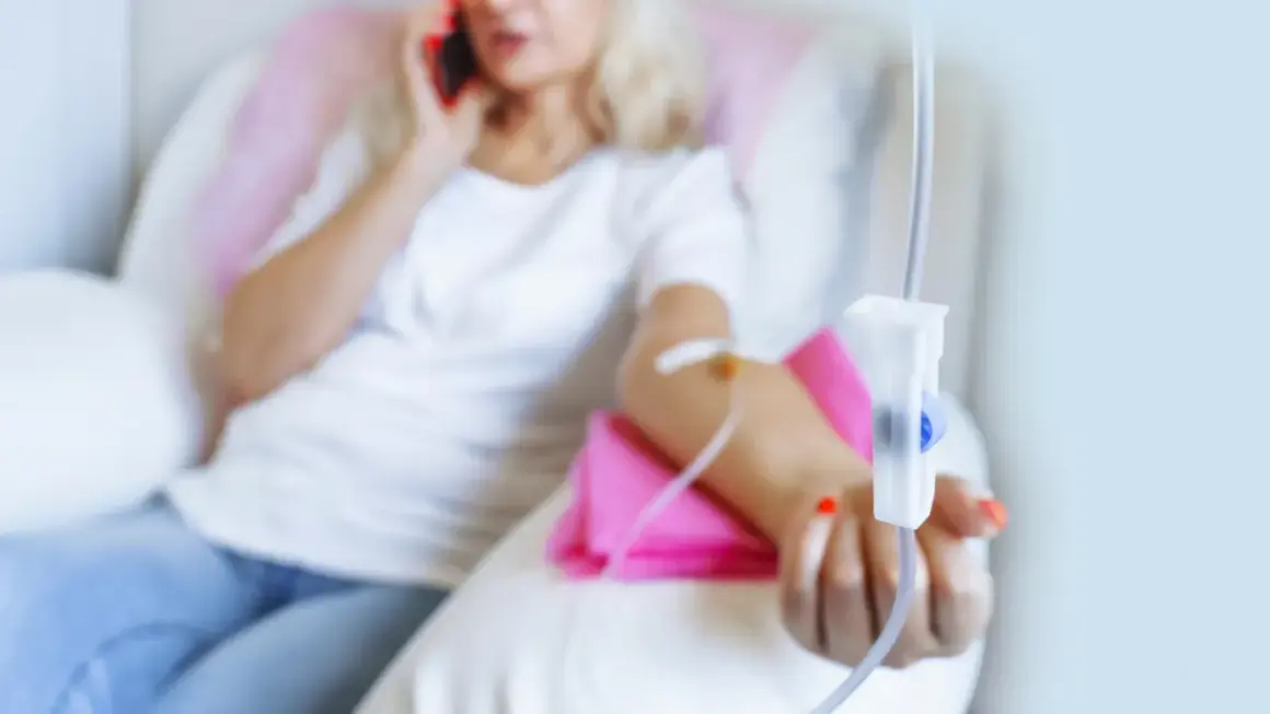 Kobieta z kroplówką w ręku rozmawia przez telefon.