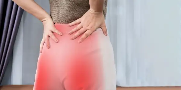 Kobieta trzymająca się za bolące biodro, z zaznaczonym na czerwono obszarem bólu.