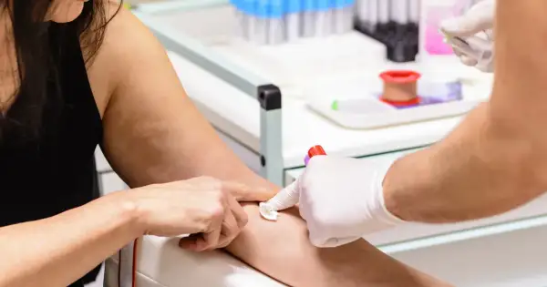 Pobieranie krwi do badań. Ręka pacjentki z wacikiem, ręka pielęgniarki w rękawiczce z igłą i probówką MPV.