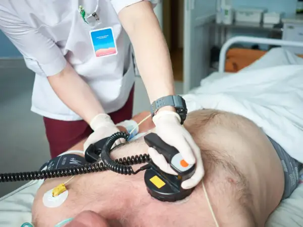 Ratownik medyczny wykonuje kardiowersję pacjentowi w szpitalu, używając defibrylatora.
