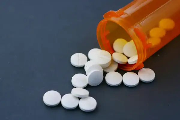 Białe tabletki rozsypane z pomarańczowego pojemnika. Niektóre z nich mogą zawierać fentanyl, substancję o silnym działaniu.