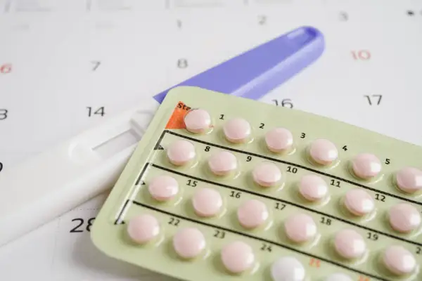 Test ciążowy i blister tabletek antykoncepcyjnych na tle kalendarza. Decyzje o płodności, planowanie rodziny, vixpo.